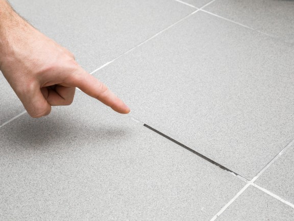 Finger zeigt auf beschädigte Fliesenfuge